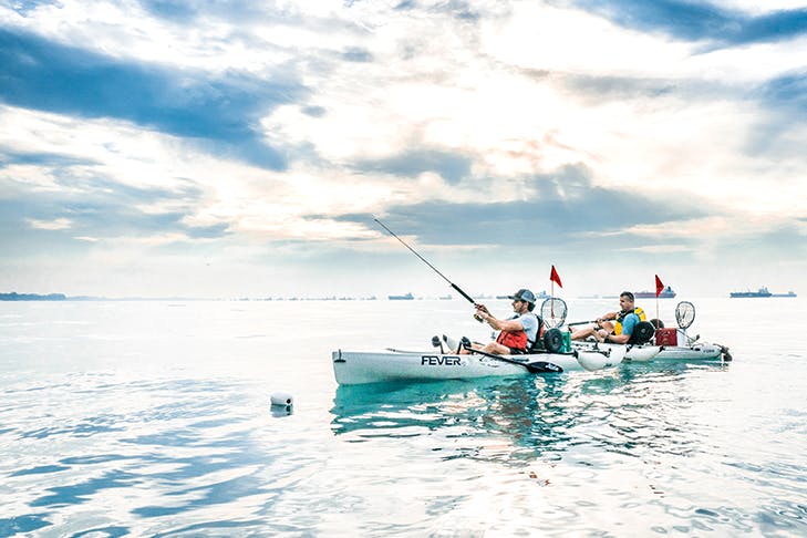 Two people kayaking with blue skies and clouds.